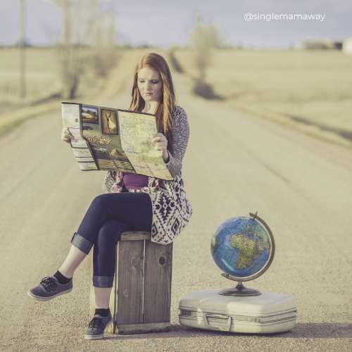 Woman sitting on a crate in the middle of a road reading a map