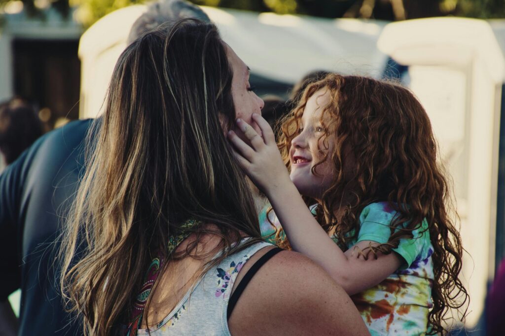 A smiling mother holding her daughter, who gently touches her face, symbolising love, healing, and new beginnings in life after divorce.