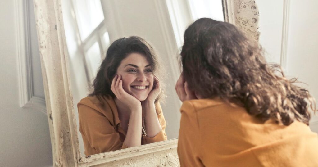 Smiling woman in mirror reflecting confidence after divorce and self-esteem rebuilding.